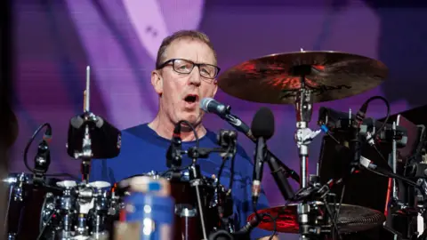 A man, Dave Rowntree, playing drums on a stage.