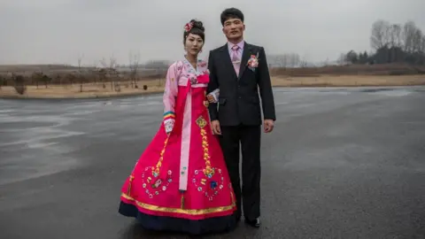 Getty  A North Korean bride wearing a traditional Korean hanbok wedding dress poses for a photograph with the groom as they arrive for a wedding party at Myrim Riding Club on February 06, 2019 in Pyongyang, North Korea