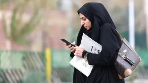 AFP A woman in Tehran with a newspaper looking at her mobile phone
