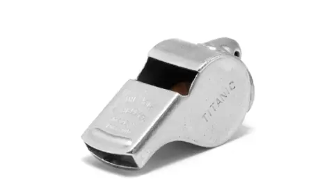 ACME Whistles A silver-coloured metal whistle sits on a white background with the word "TITANIC" engraved on its side. The whistle is an ACME Thunderer model with "ACME THUNDERER" and "MADE IN ENGLAND" stamped on the top. It has a rounded pea chamber and a flat mouthpiece, with a slightly weathered or distressed finish giving it a vintage appearance.