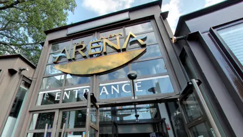 Google The entrance to the Alban Arena in St Albans is made of steel and glass with a large gold sign depicting the venue's name and the word "entrance written in white.