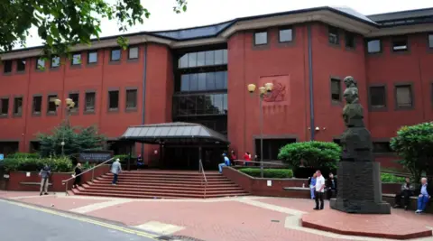 PA Media A large red brick building with steps leading to a large entrance and a number of trees, bushes and people at the front