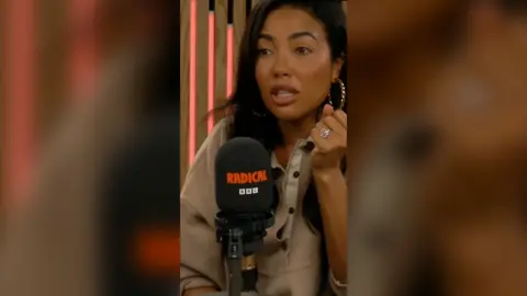 Emma Grede wearing a beige buttoned jumper. She is sat in front of a black microphone which has 'Radical' and 'BBC' on it.