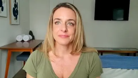 Ashley Rubright wears a green top, sitting by wooden tables.