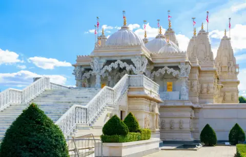 Getty Images An elaborate Hindu white stone temple with domes and turrets with gold on top. It is set against a blue sky. 