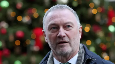 EPA/Shutterstock A man with short grey hair and a grey goatee looks at the camera 