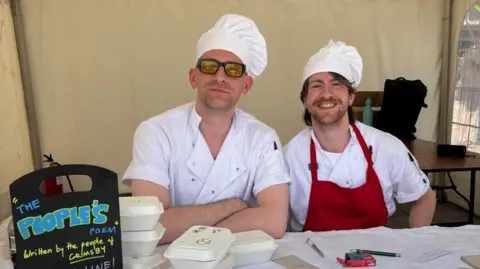 North East Lincolnshire Council Two men sat behind a table in a tent. They are both wearing chef's outfits and are smiling at the camera. 