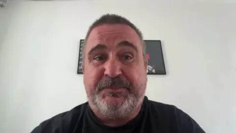 Head and shoulders picture of Andrew Smith who has a short grey beard and hair and is wearing a black t-shirt