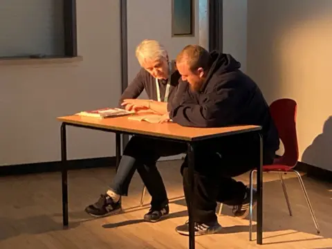 Nadia Gyane/BBC Aaron Rogers having a reading lesson from coach Anne Jones