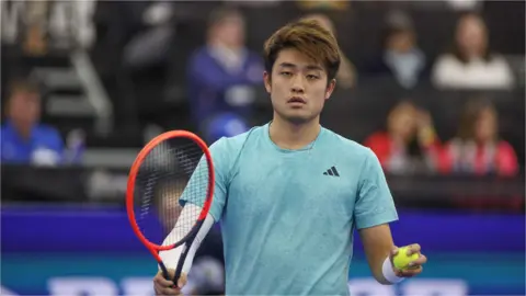 Wu Yibing holds his racquet in his right hand and a ball in his left