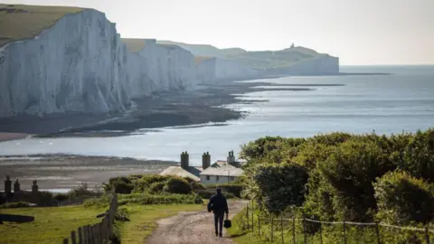 Getty Images A man walking towards the mouth of the Cuckmere River, with the Seven Sisters cliffs in the background.