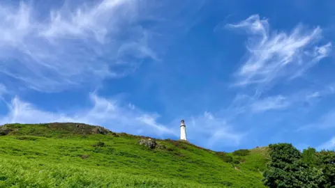 StirCrazy A white lighthouse standng on a grassy hill under a blue sky. 