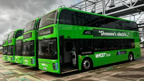 A row of new, bright green double decker buses stand at a depot in Bristol