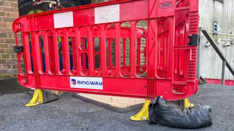 A red barrier around the drain, which has a temporary yellow cover on top of it. 