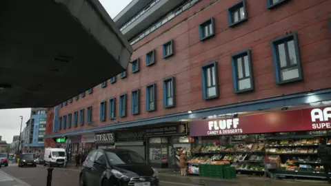 The exterior of the Arndale House student accommodation block in Liverpool. It is a seven-storey building with shops including a Tesco Express, a blinds shop and a Fluff candy and desserts store on the ground floor