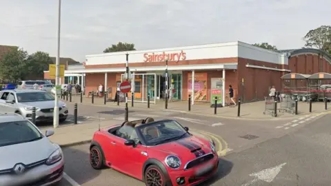 Front of a Sainsbury's supermarket on a sunny day with cars parked out the front