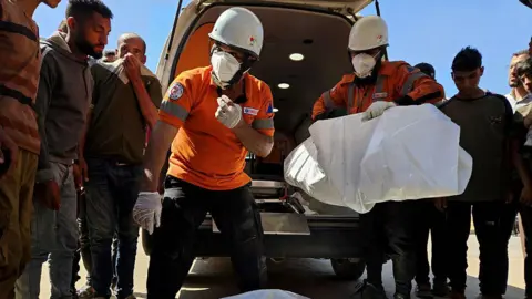 Civil defense teams carry the body of a Palestinian following an Israeli airstrike on residential areas in central Khan Yunis, southern Gaza, on May 23, 2025.