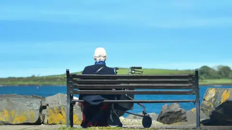 A person sitting on a bench, they have their back to the camera
