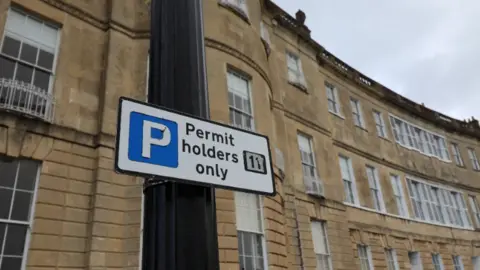 Banes A sign attached to a lamppost reading 'permit holders only' and displaying a P for parking