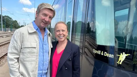 Ice skating legends Jayne Torvill and Christopher Dean standing next to a tram that has been named after them in Nottingham.