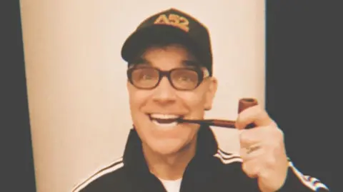 Instagram/@RobbieWilliams Robbie Williams is wearing Eric Morecambe's glasses and posing with his pipe in his mouth.
