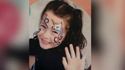 Love, Jasmine A young girl, Jasmine, smiles and waves with face paint on.