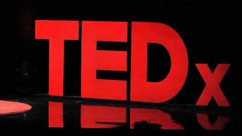 A TEDx red sign that sits on a stage during a talk. 