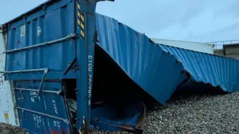 Donna Tretheway A broken up blue shipping container on its side on the pebbled beach.