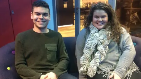 BBC Josh Tapper with short dark hair wearing a green top and Amy Tapper with long brown hair wearing a large scarf