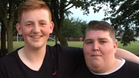 Family handout A man with short red hair has his arm around a woman with short brown hair. They are both smiling. They are standing outside with trees and grass behind them.