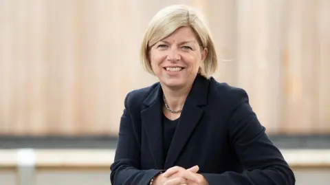 Ringwood School Leanne Symonds smiles at the camera with herhands together. She has short blond hair and is wearning a navy jacket. 
