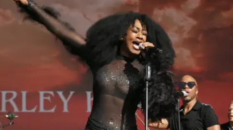Beverley Knight performing at Godiva Festival 2024. Her right arm is outstretched and her left arm is holding a microphone.
