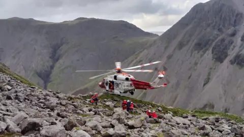 Wasdale MRT Volunteers help a casualty walk to as helicopter hovering among steep hills