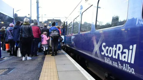 Passengers queue up to board a ScotRail train