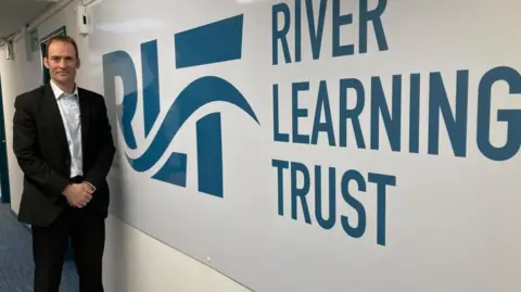 A man is standing to the left. Next to him, in big letters, says River Learning Trust