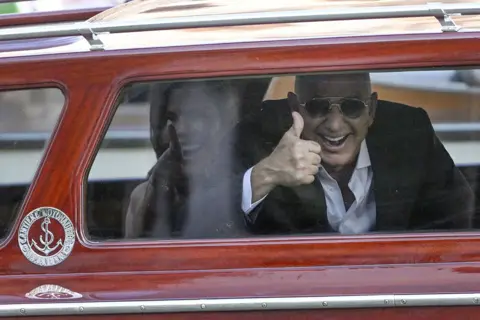 Getty Images Amazon founder Jeff Bezos and Lauren Sanchez gesture from the taxi boat at the Aman Hotel in Venice on June 26, 2025.