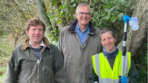 Peter Shallcross, Chair of the Nadder Valley Farmers Group, Councillor Richard Budden and Tracy Adams, Farm Conservation Advisor stand under a tree all looking at the camera