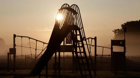 A stock image of a children's playground. There is a climbing wall and a slide in the image.