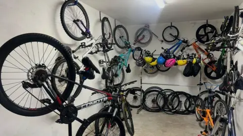 A room with bikes hanging on the walls. There are also yellow, blue, and pink helmets on the wall.