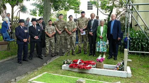 The Jersey Field Squadron Militia A group of people including four members of the military are standing by Sapper Onions' grave.