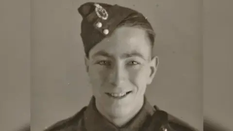 John Maskell is photographed during World War Two in his uniform. The photo is sepia coloured, Mr Maskell is smiling.