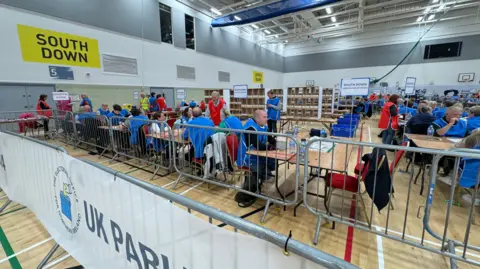 BBC election count centre staff sit behind railings waiting for ballot boxes to arrive