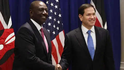 AFP via Getty Images US Secretary of State Marco Rubio (R) and Kenya's president William Ruto (L) shaking hands with Kenyan and the US flags on the background