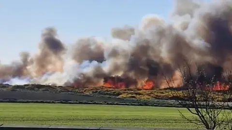 A large fire across a field with lots of grey smoke in the sky 