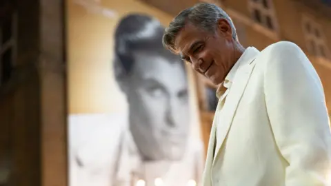 Netflix George Clooney in Jay Kelly, wearing a white suit and smiling at the gound