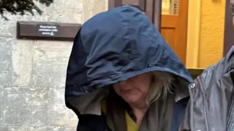 PA Media Jane Barnard looks to the ground as she leaves Gloucester Crown Court, her face is obscured by the navy blue hood of a rain jacket
