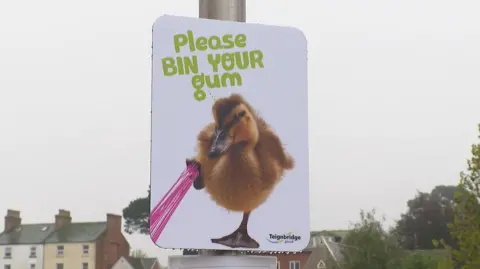 BBC A poster saying "Please bin your gum" which shows a generated image of a duck with gum stuck to its foot