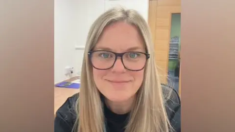 Supplied A woman with blonde hair. She has big glasses and is wearing a black t shirt. 