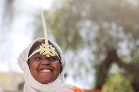 EPA A woman wearing a palm headdress smiles.