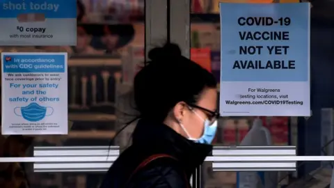 Getty Images A woman walks past a "Covid-19 vaccine not yet available" sign outside a store in Arlington, Virginia on December 1, 2020